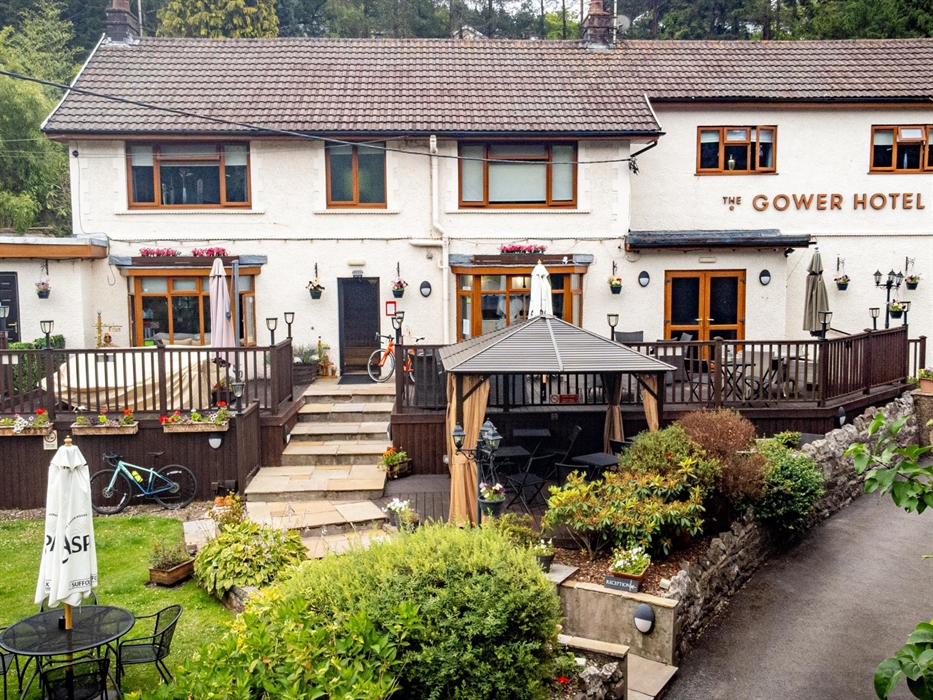 Hotel with gardens and outside seating area with tables, chairs and umbrellas