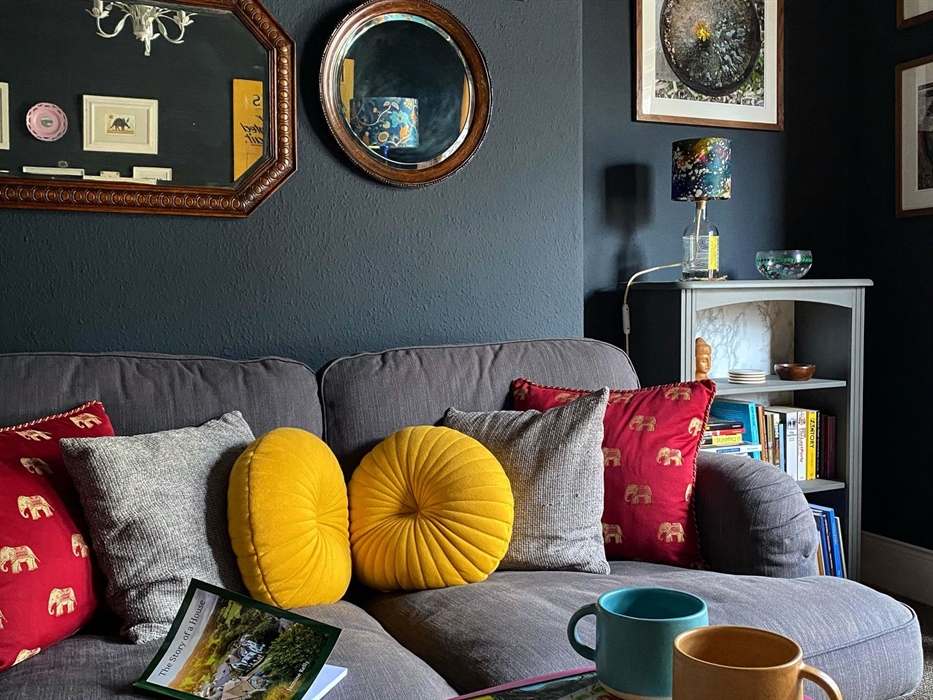 grey sofa against a black wall with yellow and red cushions, and mirrors above it
