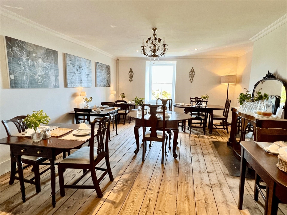 The breakfast room with it's original floorboards is decorated with a mix of antique Pembrokeshire tables and modern art and the sash window over look