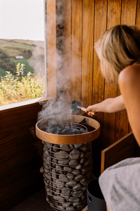 Person putting water on hot stones in sauna at Welsh Lavender
