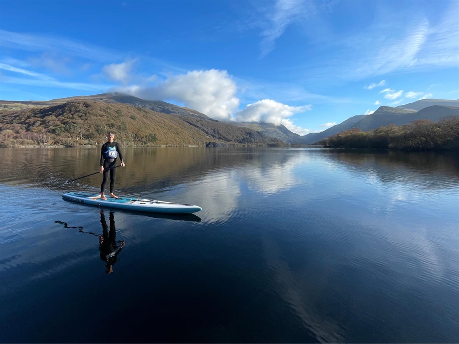 Picture of a man on a paddleboard with flat water and mountains in the background.