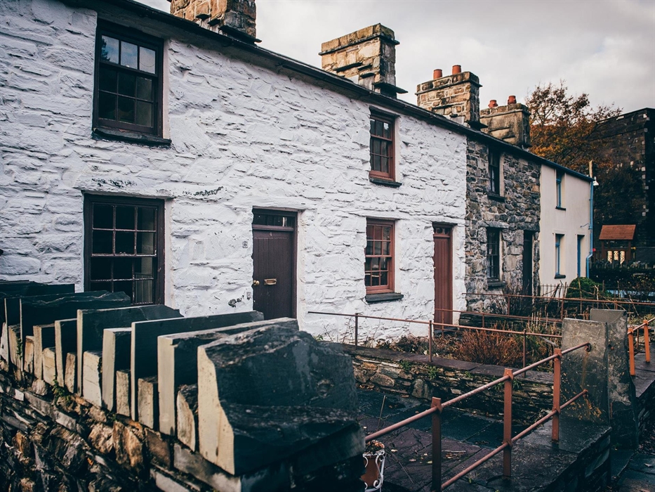 A row of 4 small cottages, built of stone. The first two cottages are painted white. They have one window and a door downstairs and one window upstair