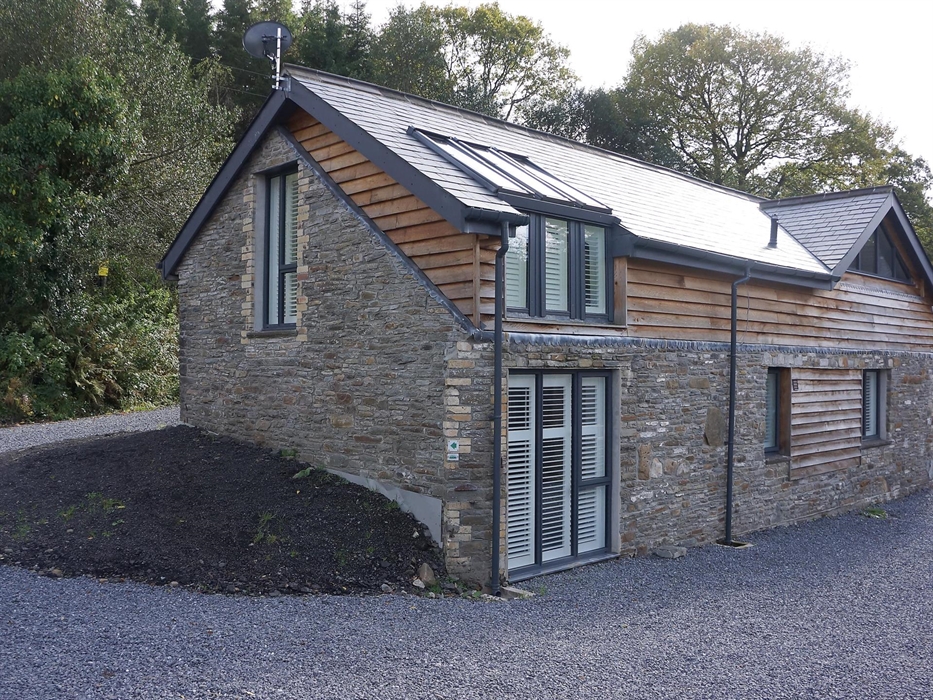 Exterior of Ty Gambo showcasing traditional Welsh stone and contemporary timber cladding, with large shuttered windows.