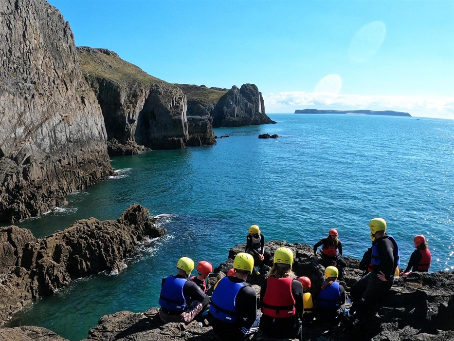 A group of coasteerers listens to their pre-session brief on a rock at Lydstep.
