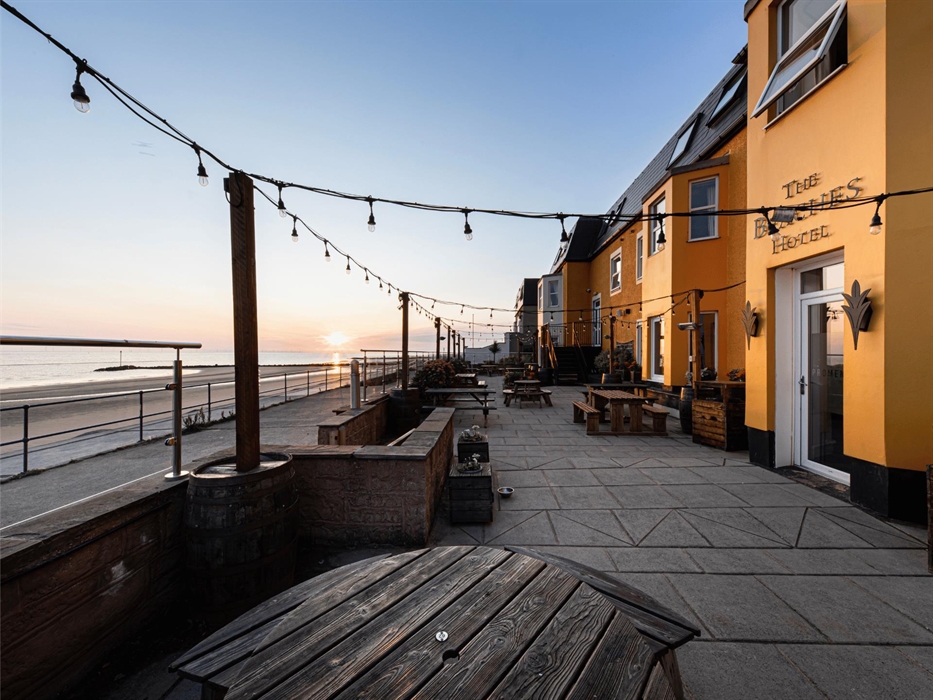Seating area on the promenade Terrace overlooking the beach and Irish Sea. The back of the hotel painted a sunny yellow.