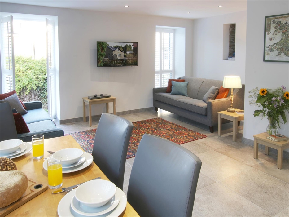 Spacious and bright open-plan lounge and dining area with two sofas, a flat-screen TV, and a set table.