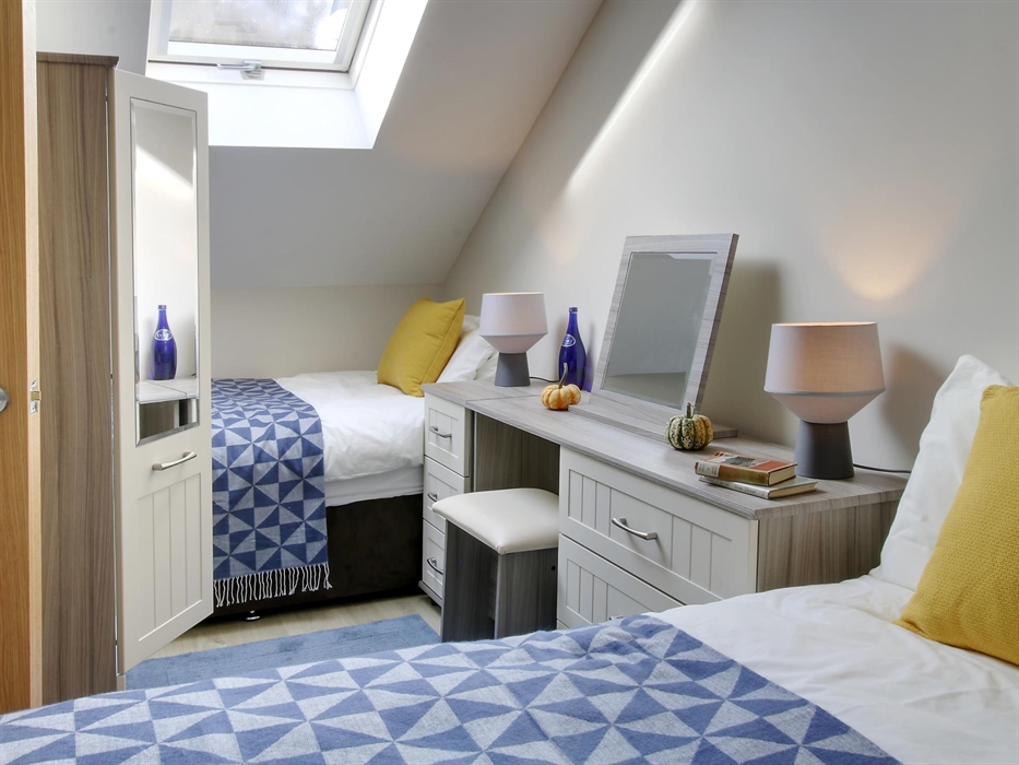 Bright attic twin bedroom with a skylight, blue patterned throws, and a dressing table with mirror and lamps.
