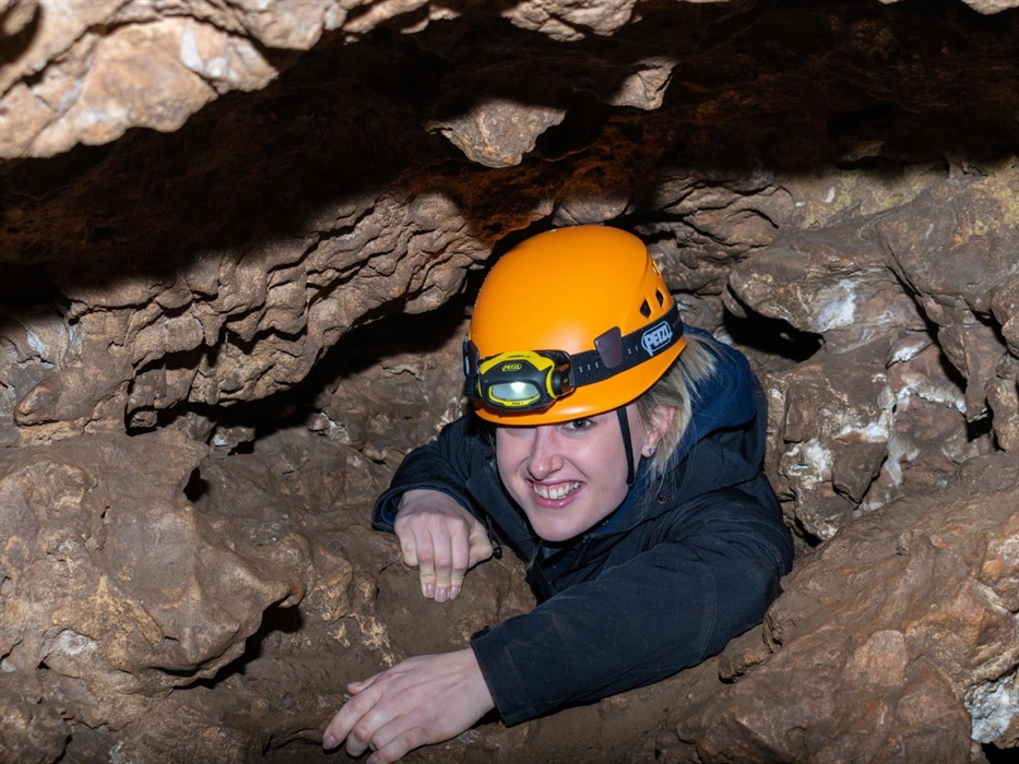 Lady wearing helmet crawling up through cave