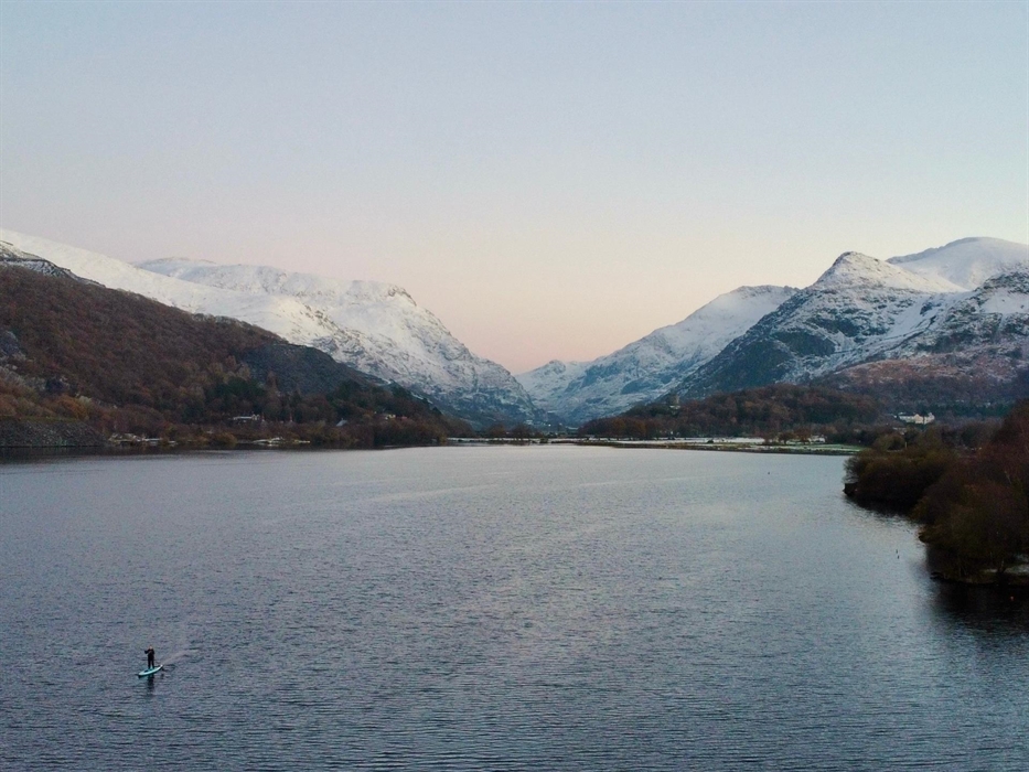 Picture of a lone paddleboarder on a welsh lake with snowy mountains in the background