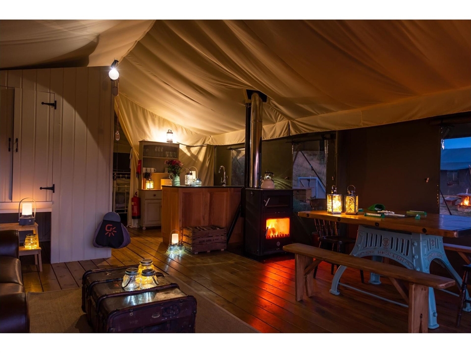 The lounge and dining area of the inside of Afon safari tent, with trunk coffee table, the fire light and dining table in the foreground