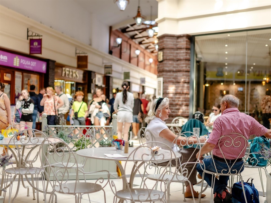 Two people sat at a table enjoying refreshment from a cafe in the busy mall of the Victoria Centre