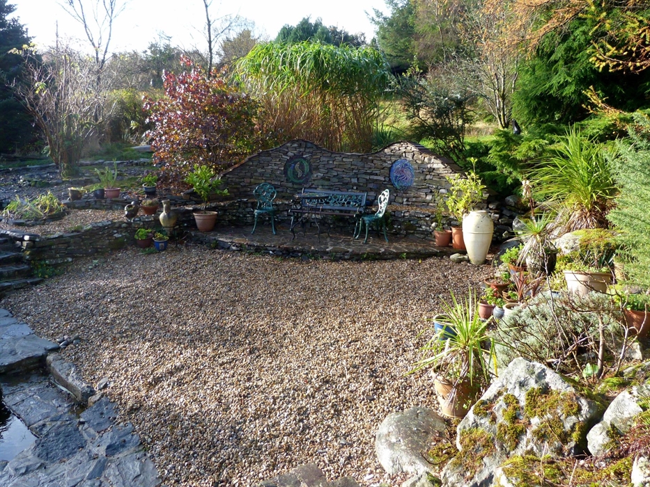 A garden depicting Spain, with a patio featuring mosaics, large pots, a pebble beach and spiky plantings