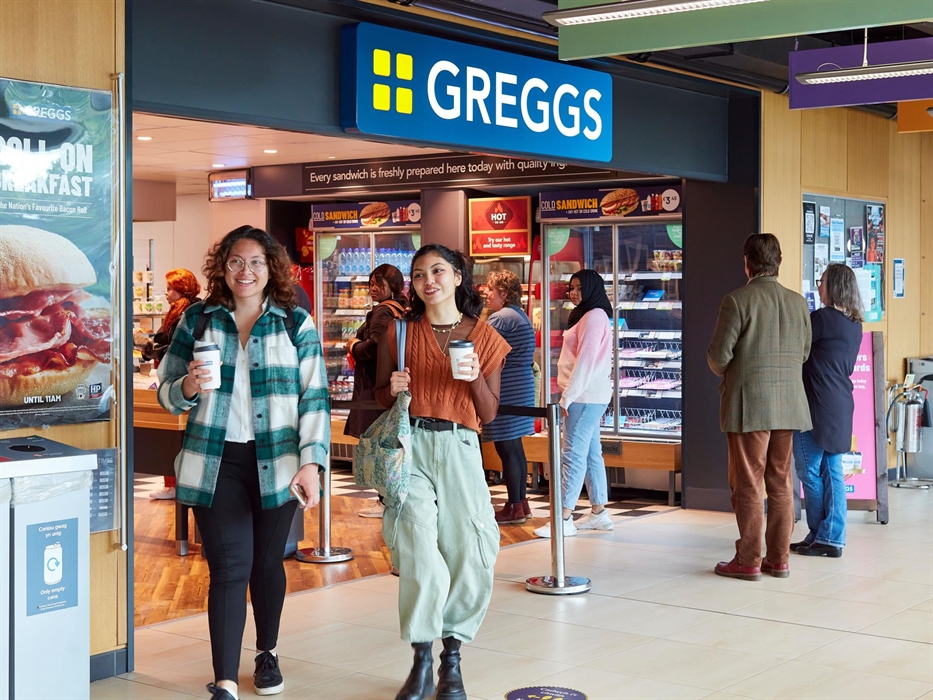 Students leaving the greggs on campus carrying coffee