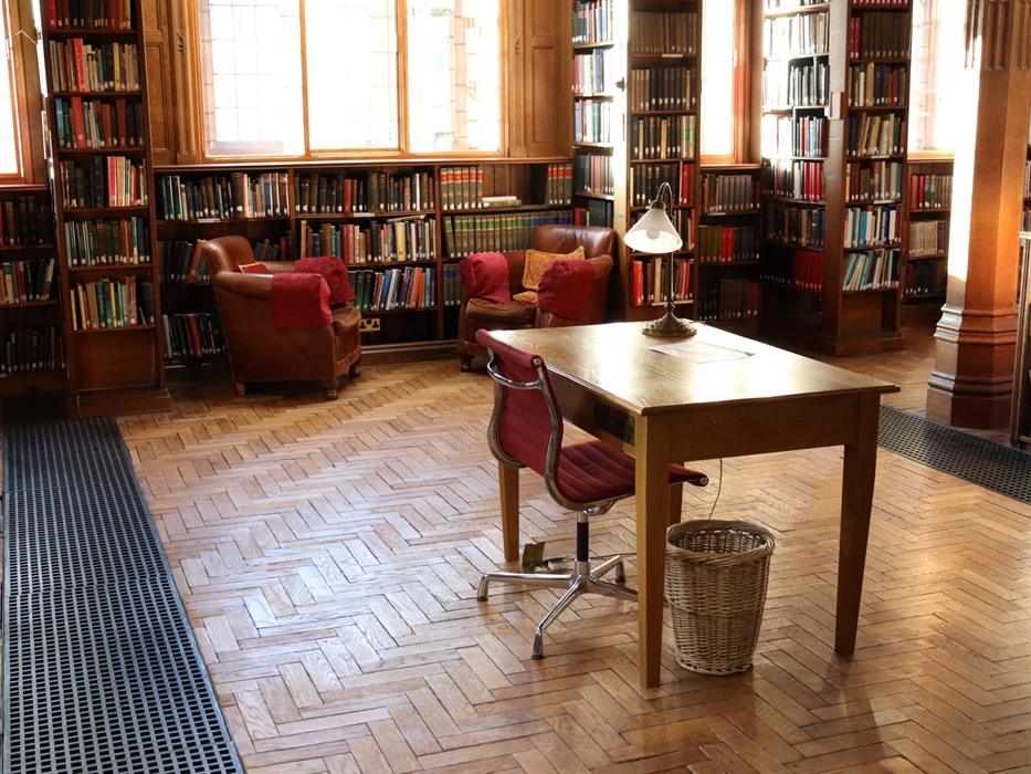 A Desk in the Reading Rooms. It's a small wooden desk with a small lamp atop it. There's a red seat beneath the desk.