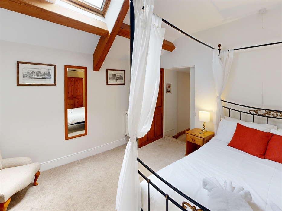 Bright master bedroom featuring a four-poster bed, skylight, and traditional furnishings.