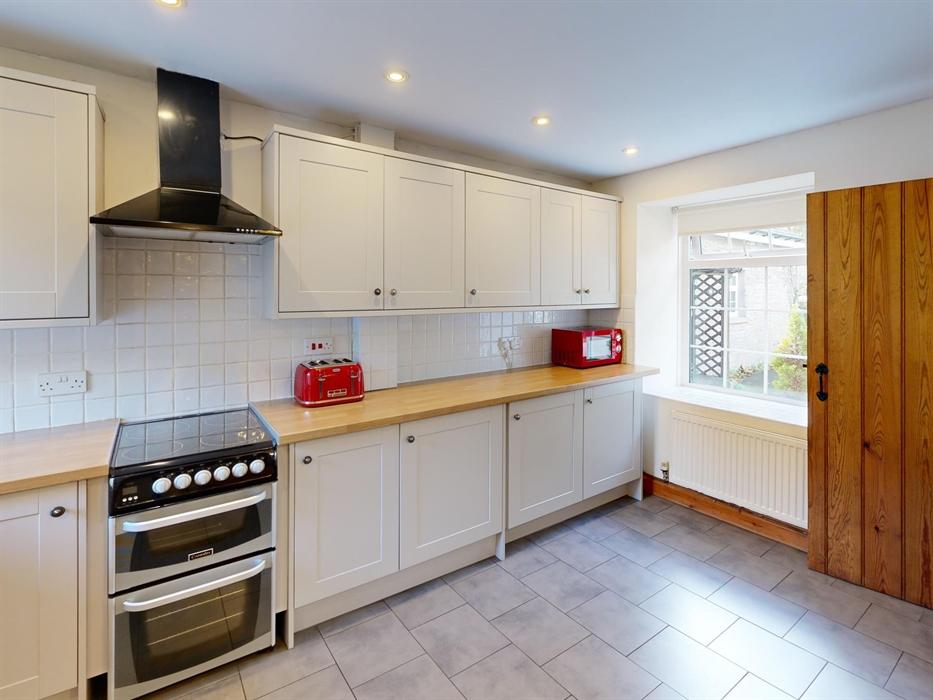 A clean, modern kitchen with integrated oven, bright red toaster and microwave, and views onto the cottage garden from a wide window.