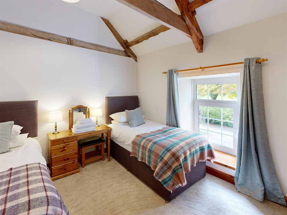 A twin bedroom with high vaulted ceilings and exposed beams, featuring two single beds with soft throws and a wooden dressing table between.