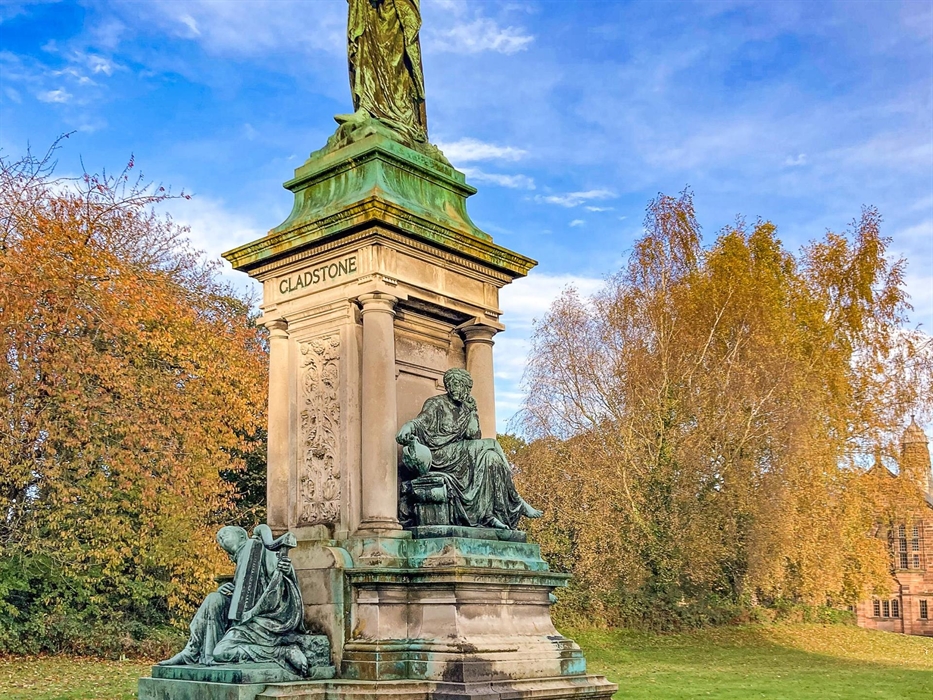 A statue of William Gladstone (green copper) on a tall plinth. Mythological figures surround the base.