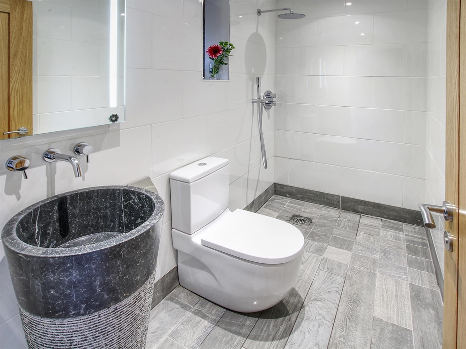 Contemporary bathroom featuring a striking black stone basin, rainfall shower, and sleek white tiling.