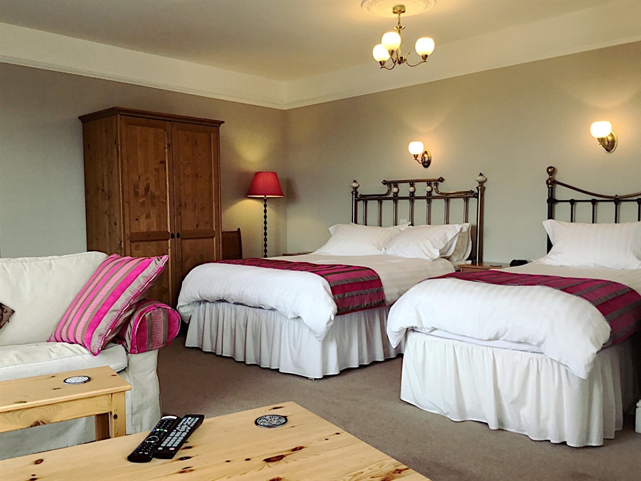 Twin room showing a double bed and a single bed with lamps over the beds and a sofa and coffee table visible in the foreground