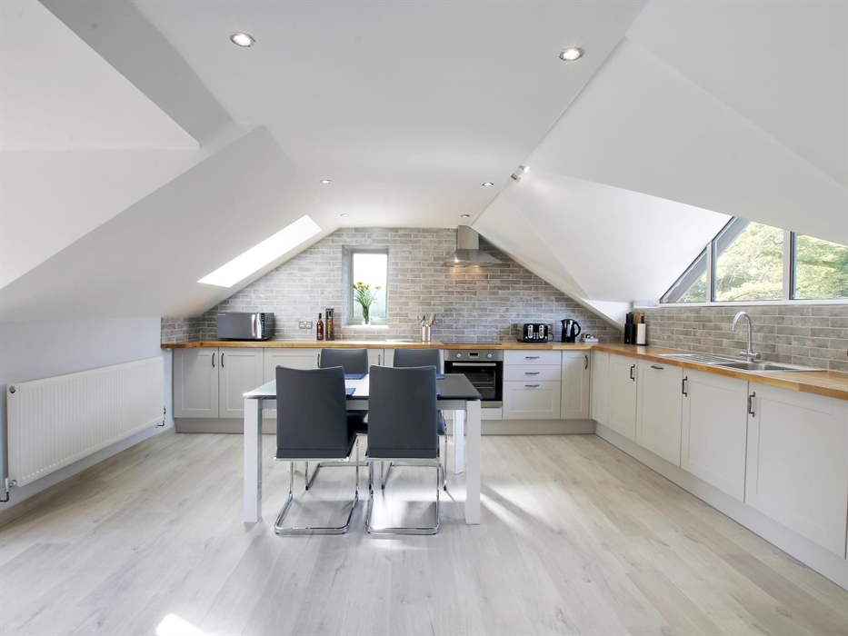 Modern open-plan kitchen with white units, wooden countertops, and vaulted ceilings featuring skylights and grey brick-style tiles.