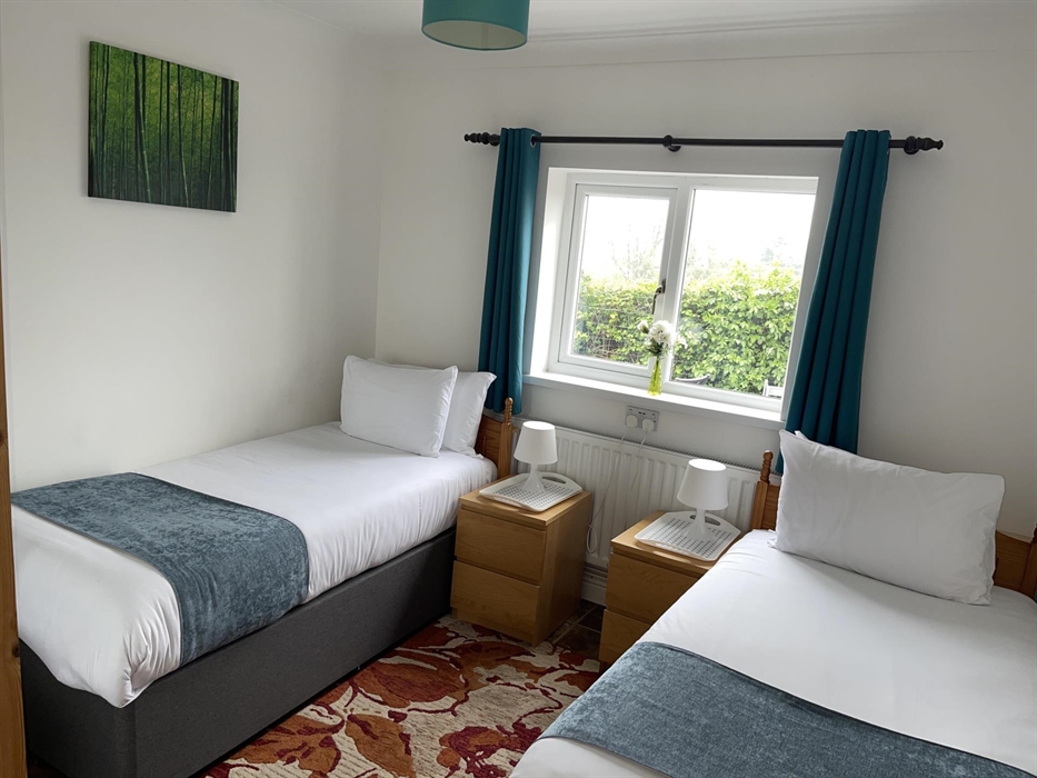 Twin bedroom with 2 full size single beds, 2 bedside cabinets, mirror wardrobe and window overlooking the private garden area