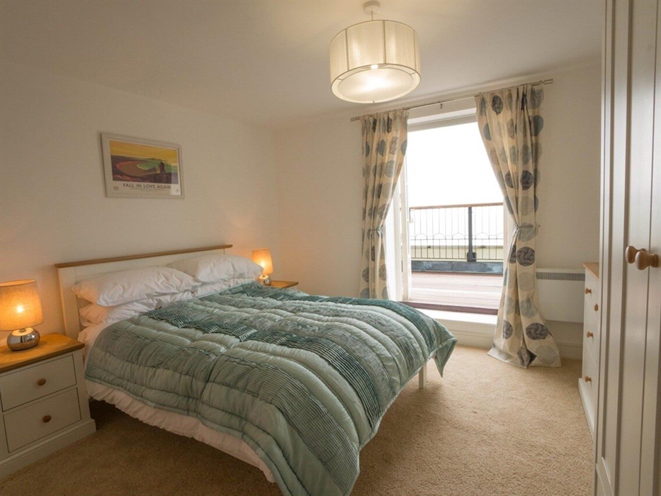 Front of apartment bedroom with king bed and bedside cabinet and bedroom furniture with open door onto balcony