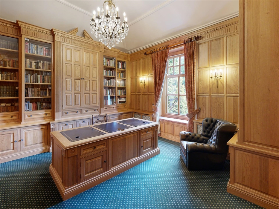 Stately home library at Plas Cilybebyll with floor-to-ceiling bookshelves, oak paneling, a large central desk, chandelier, and a leather reading chair