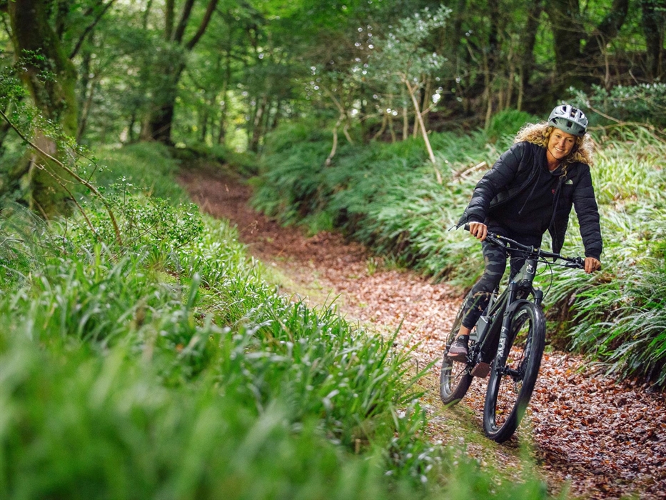 Cyclist rides downhill with a smile on their face in the forest in Cwm Gwaun.