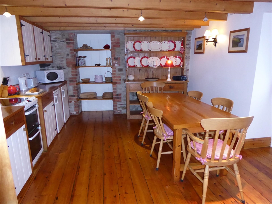 A wooden dresser adorned with red and white plates brightens this farmhouse style kitchen. The six chairs with red gingham seat pads sit comfortably a