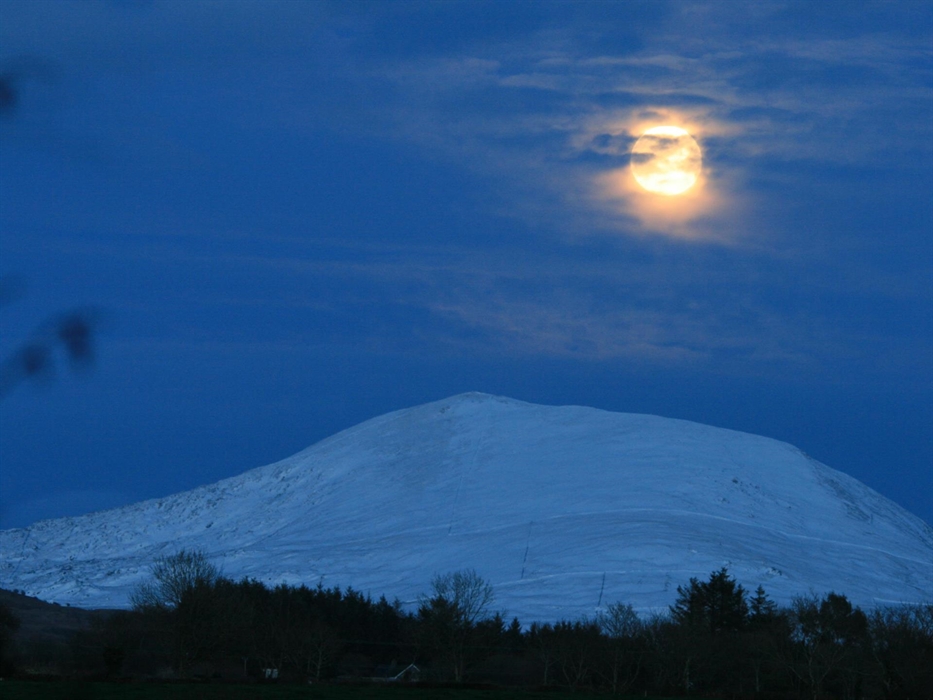 Snow covered mountain Moel Hebog under the moonlight. An area of Dark Skies