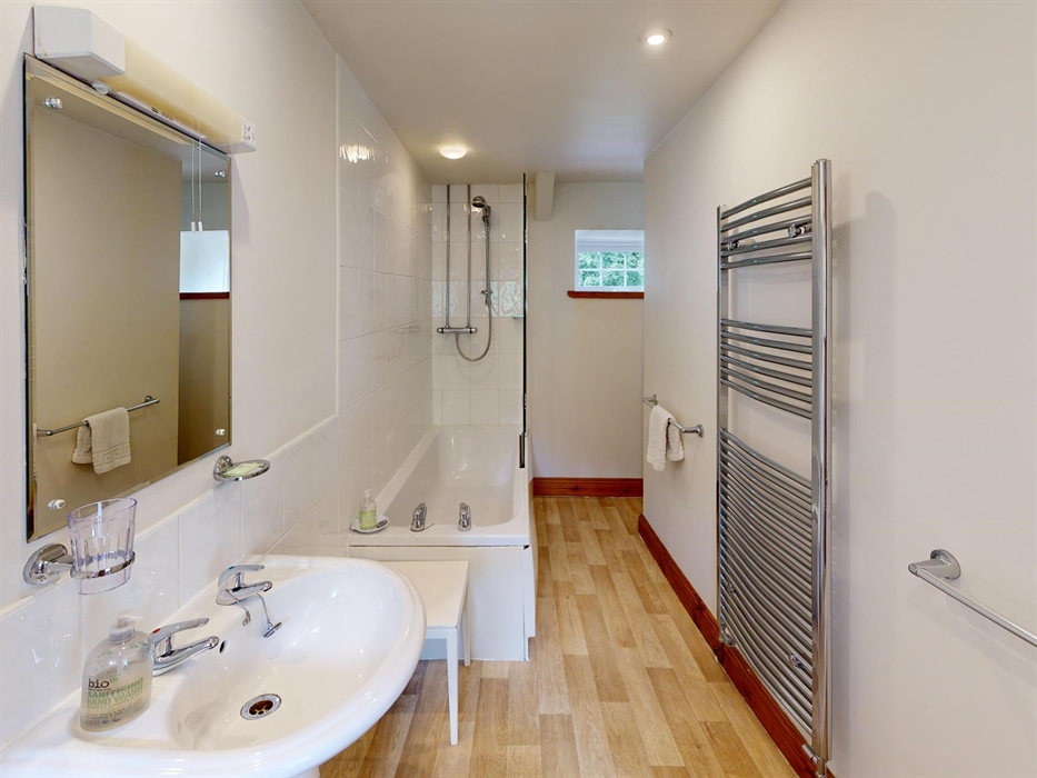 Clean, modern bathroom with bath, overhead shower, large mirror, and heated towel rail.
