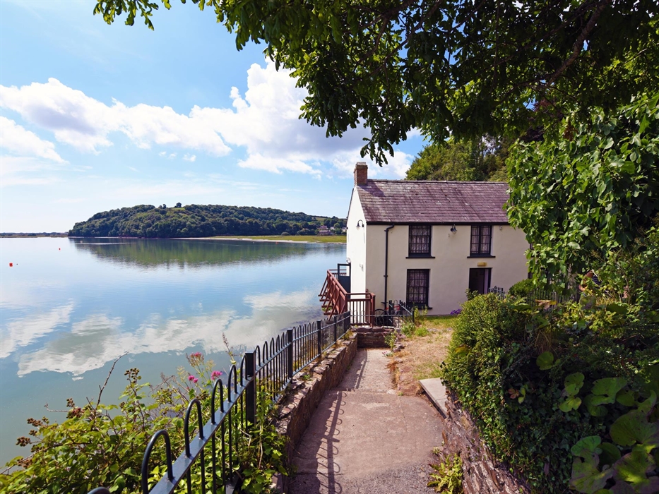 Dylan Thomas Boathouse surrounded by trees on one side and the Taf estuary on the other