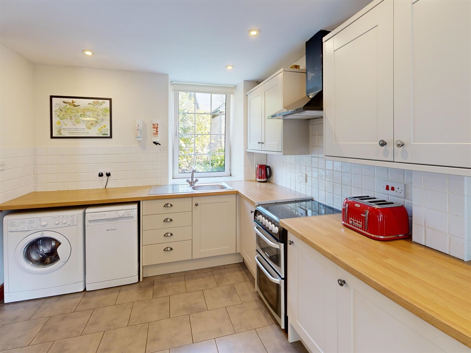 A light-filled kitchen featuring a cooker, wooden worktops, cream shaker cabinets, and essential appliances including washing machine and dishwasher.