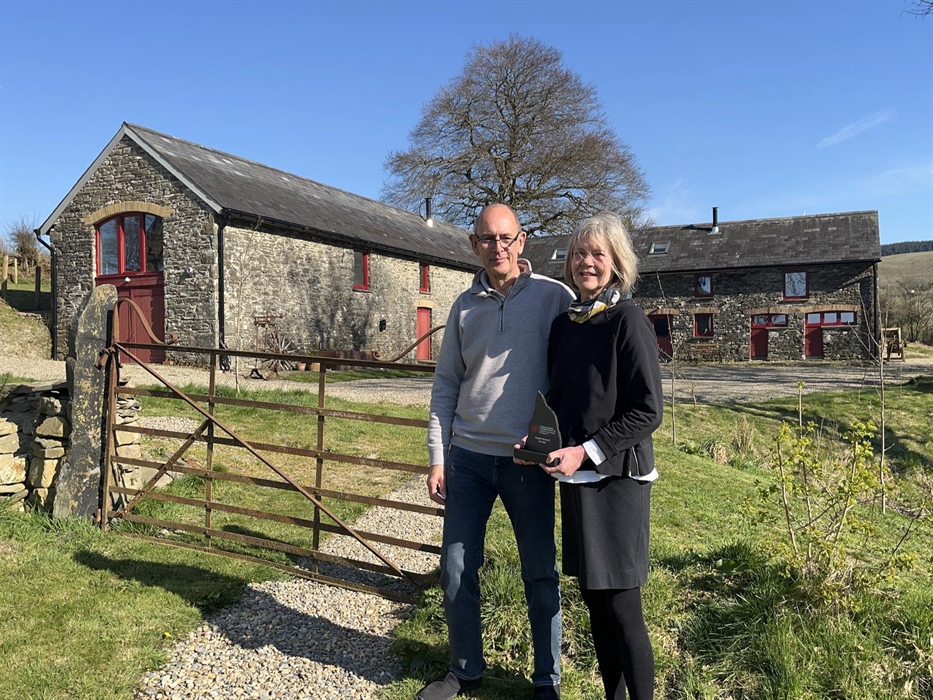 A view of the owners in front of the barn, holding their National Tourism Award for Wales 'Bro y Byd' trophy