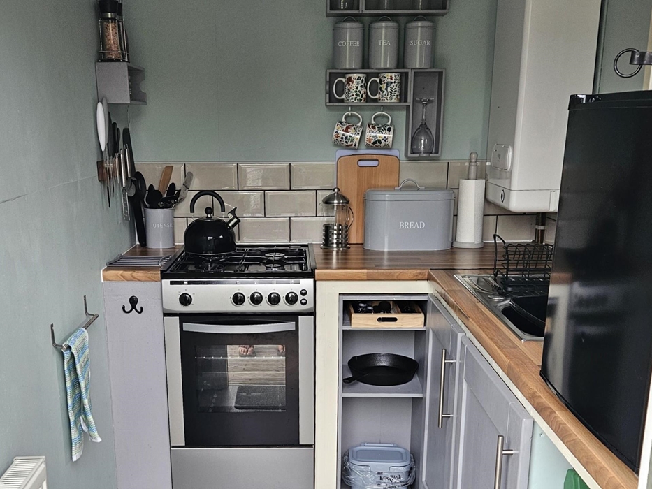 Gas cooker with hob top kettle, boiler, sink, and counter top fridge. Various equipment and utensils in container and on wall magnet, cast iron frying
