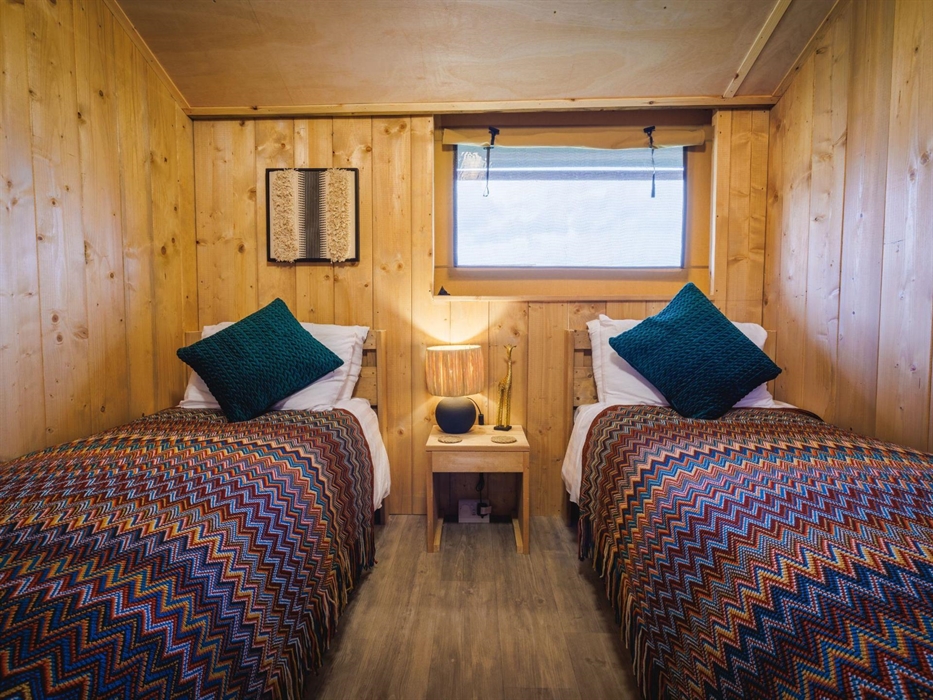 Twin single beds with African styled bedspreads, wall art and table lamp, bedside table and giraffe ornament