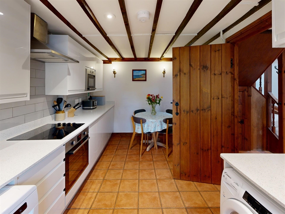 A spacious kitchen with beamed ceiling, modern appliances, and a round table with fresh flowers.