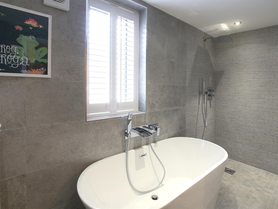 Sophisticated bathroom with textured grey tiles, a large freestanding bathtub, and a walk-in rainfall shower.