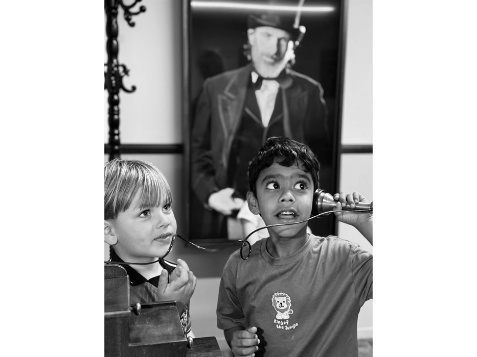 A black and white photo of two young children interacting with an old telephone from the 1800s and a picture of an industrial factory owner of the sam
