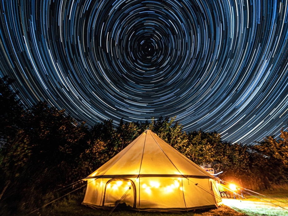 Our bell tent nestled in the wildflower camping meadow, glowingly lit with fairy lights with awesome starry skies in a halo above