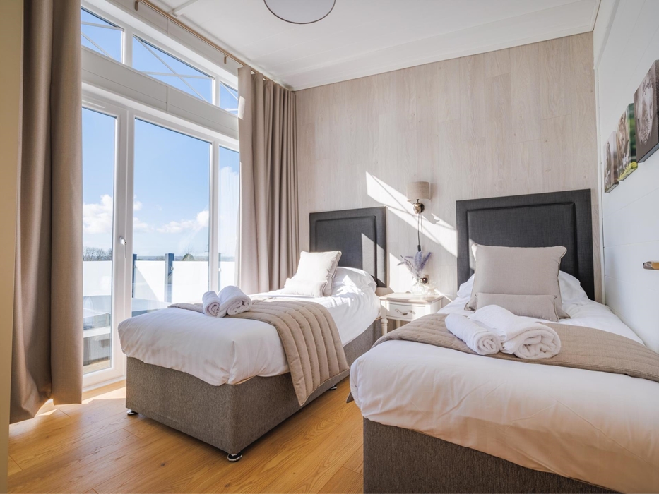Two full size single beds with grey fabric headboards and beige curtains and bed runners, a rhino head bedside lamp and rhino canvasses on the wall.