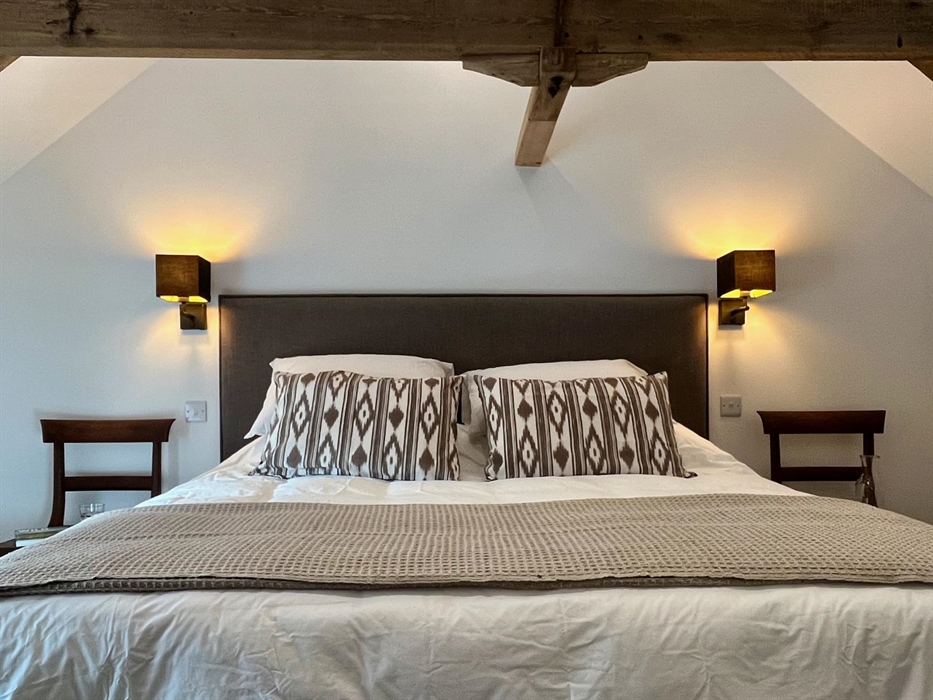 The main bedroom includes a king size bed with wall lights and chairs either side and original roof truss above.