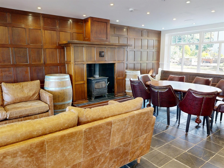 Stylish lounge featuring leather sofas, a log-burning stove set in wood paneling, and a large dining table with upholstered chairs.