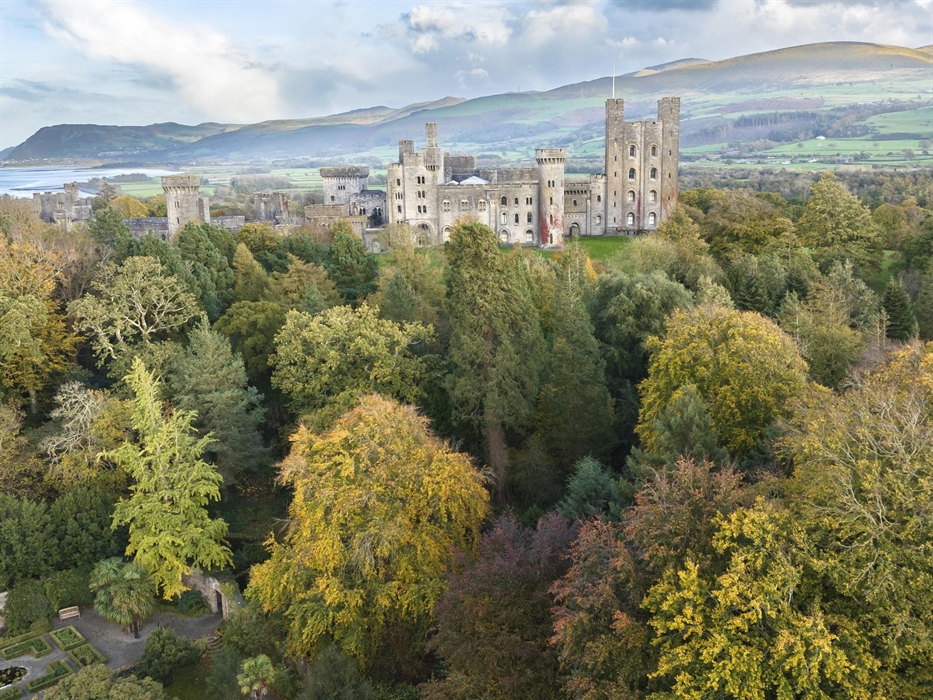 Aerial shot of Penrhyn Castle surrounded by golden and green trees in the autumn