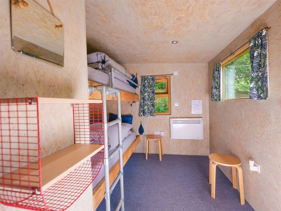 inside a wooden cabin with bunk beds, a ladder made of scaffolding, two windows with curtains and on the walls there is a small shelf, a mirror and a