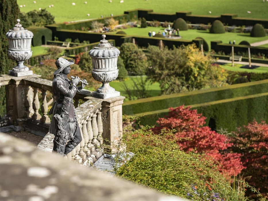 A lead statue on a stone terrace looking out onto green gardens with a long box hedge
