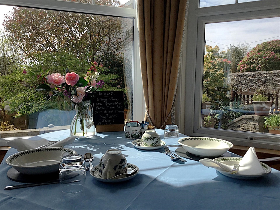 Dining table set for two with Portmeirion crockery, looking through a bay window over the garden