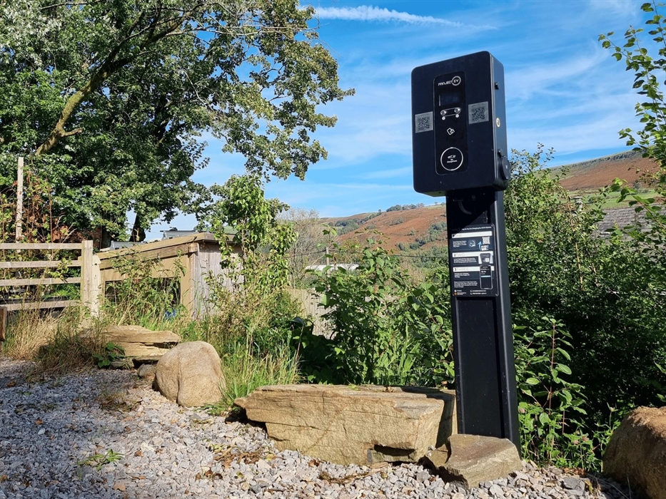 an electric vehicle charger standing by rocks and surrounded by shrubs and trees with blue sky
