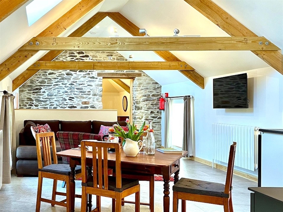 The comfortable lounge area in Y Llofft Stabl has a vaulted ceiling, exposed beams and stonework